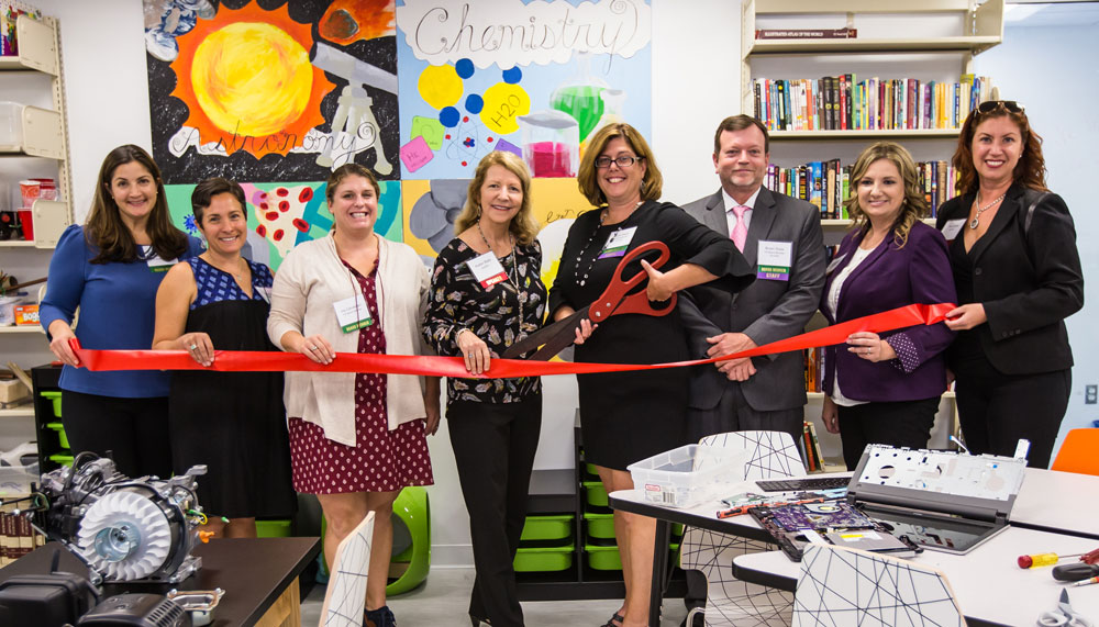 Standing in a colorful classroom with art and books on the walls, Karyn Ewart and supporting staff excitedly cut a giant red ribbon signifying The Sycamore School's Grand Opening.