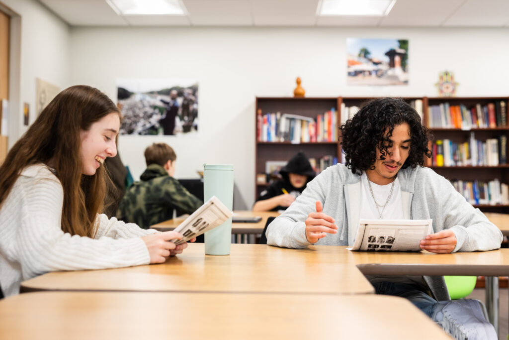 two high school students smiling as they work on a team project for class.