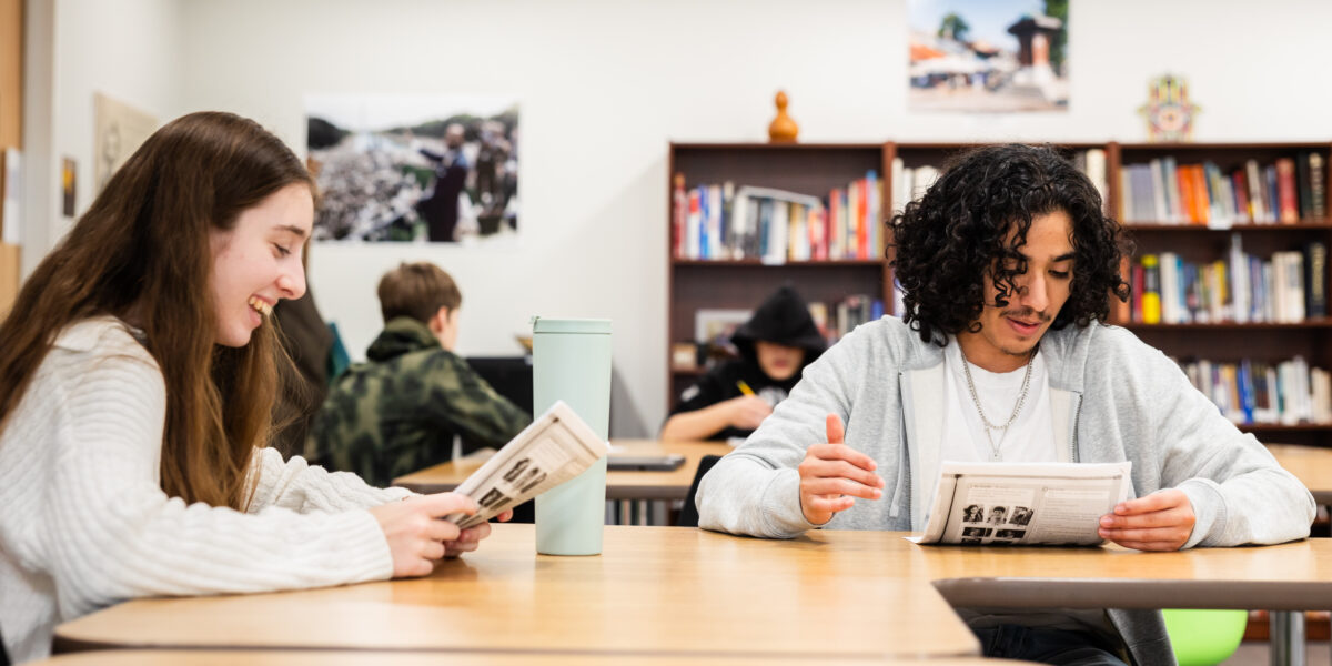 two high school students smiling as they work on a team project for class.