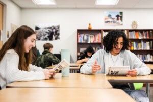 two high school students smiling as they work on a team project for class.